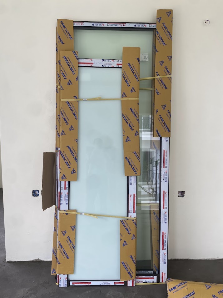 Cửa kính khung nhôm Fancydoor mới, còn bọc carton và đặt tựa tường chờ lắp đặt